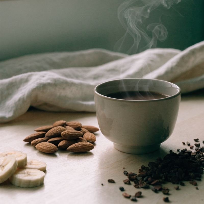 Taza de cacao caliente con almendras, plátano y cacao sobre madera