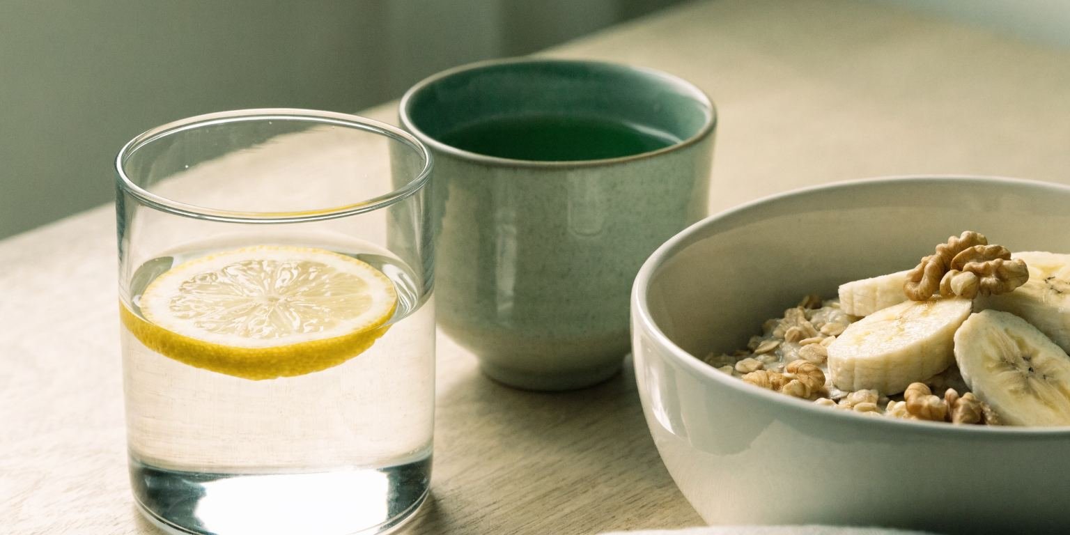 Desayuno con avena, plátano, nueces, agua con limón y té verde con luz de mañana